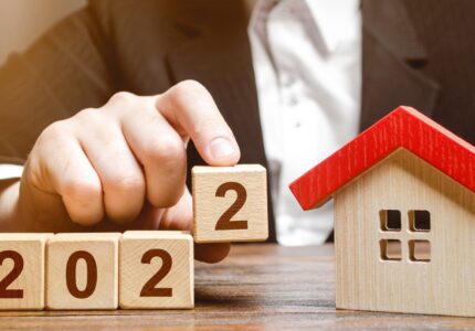 A businessman making 2022 out of blocks near house. Concept of the real estate market in the new year. Forecast of prices and offers, new trends and tendencies. Investment plans. Mortgage loan.