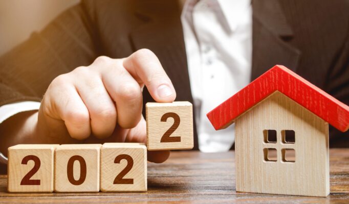 A businessman making 2022 out of blocks near house. Concept of the real estate market in the new year. Forecast of prices and offers, new trends and tendencies. Investment plans. Mortgage loan.